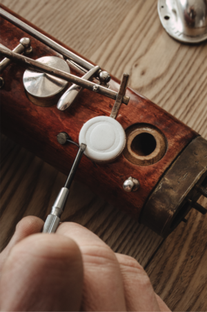 Naprawa fagotu – ręka trzymająca narzędzie precyzyjnie dostosowujące klapę drewnianego korpusu instrumentu.